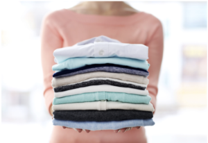 woman holds a stack of neatly folded shirts