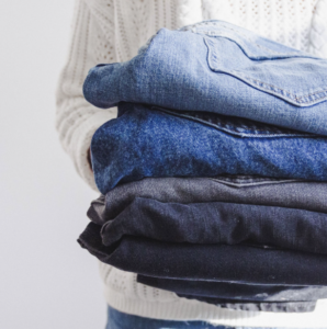 Torso of woman in white sweater holds stack of jeans