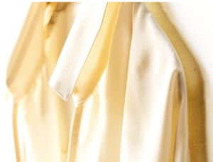 Yellow silk blouse hangs against a white backdrop